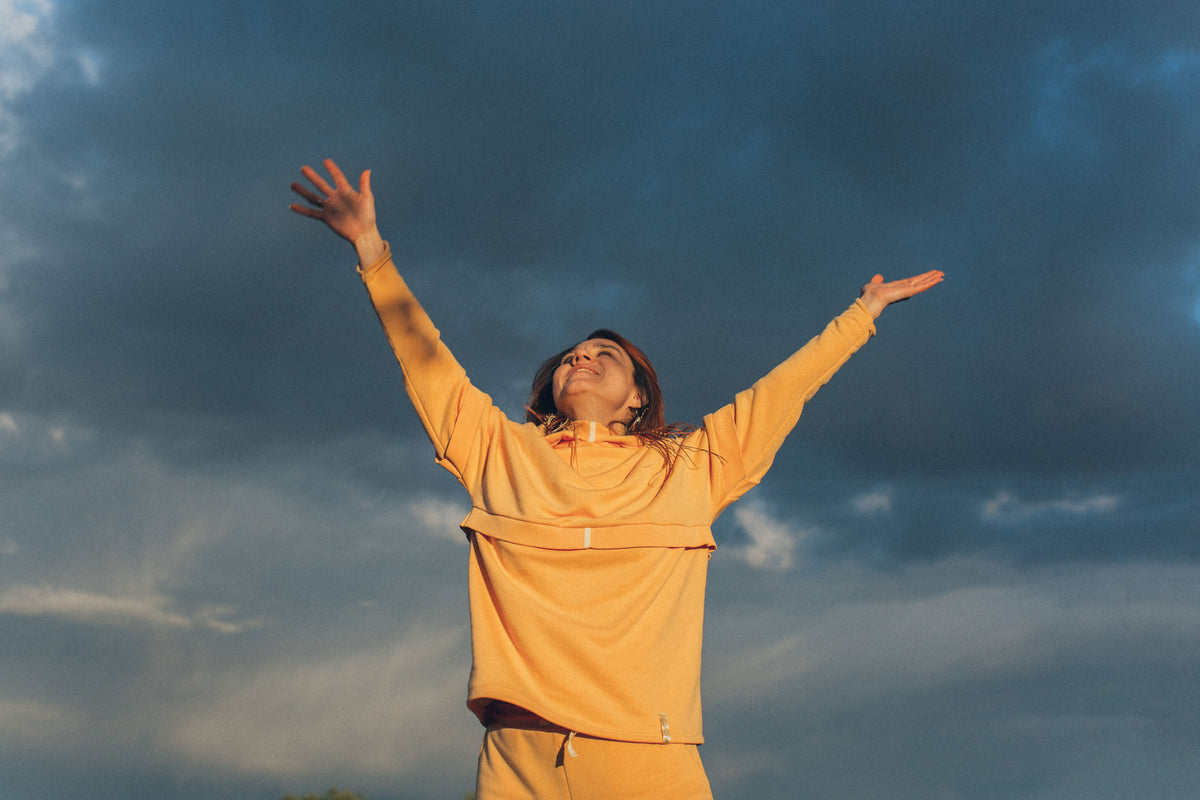 From below of anonymous joyful female in yellow clothes standing with outstretched arms against sky during summer evening in nature